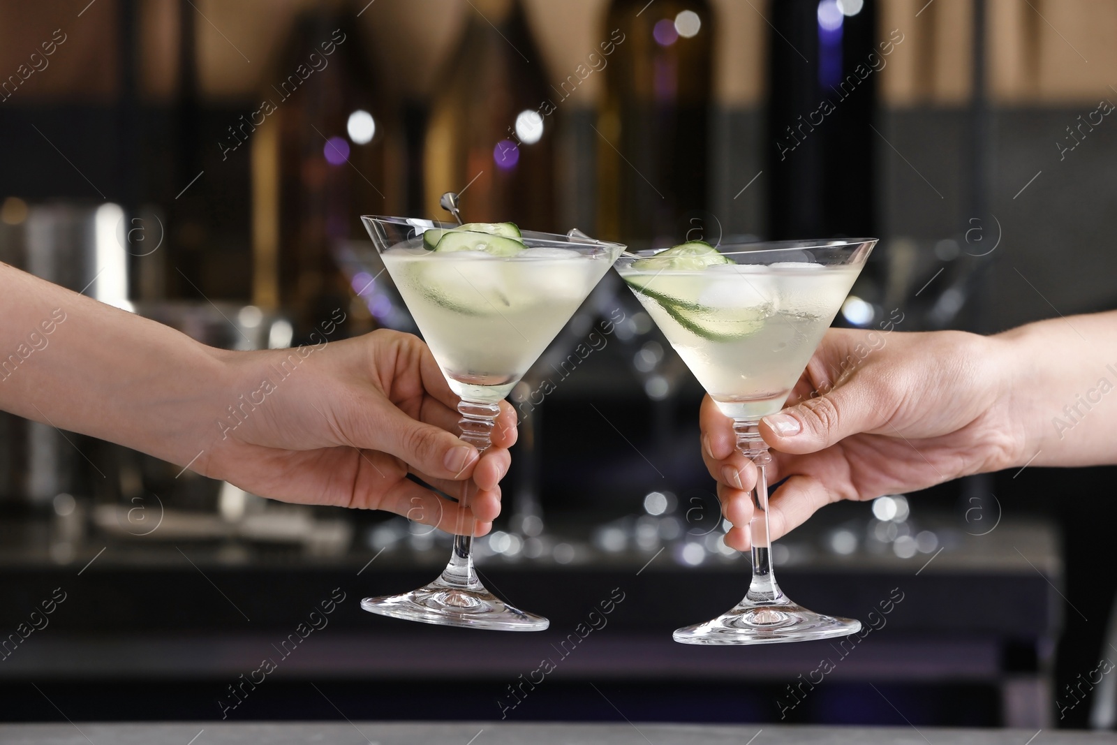 Photo of Young people clinking glasses of tasty cucumber martini in bar, closeup