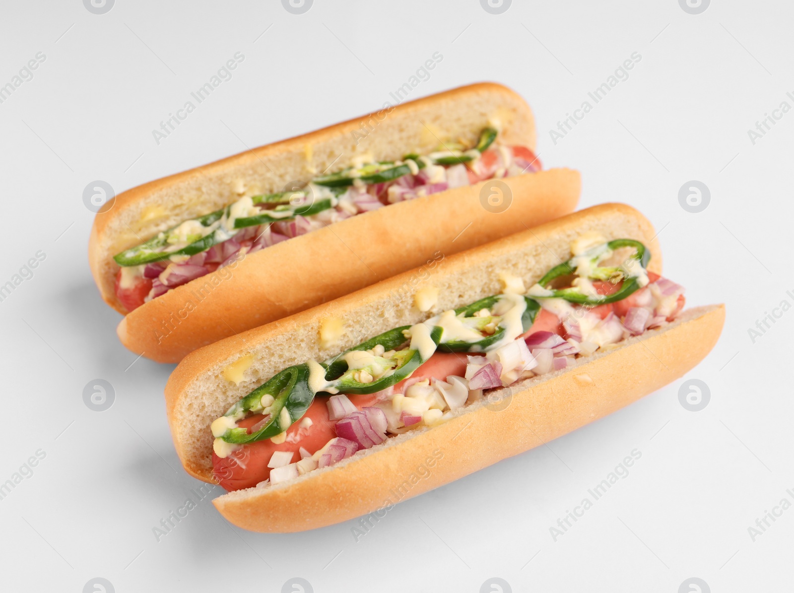 Photo of Delicious hot dogs with onion, chili pepper and sauce on white background, closeup
