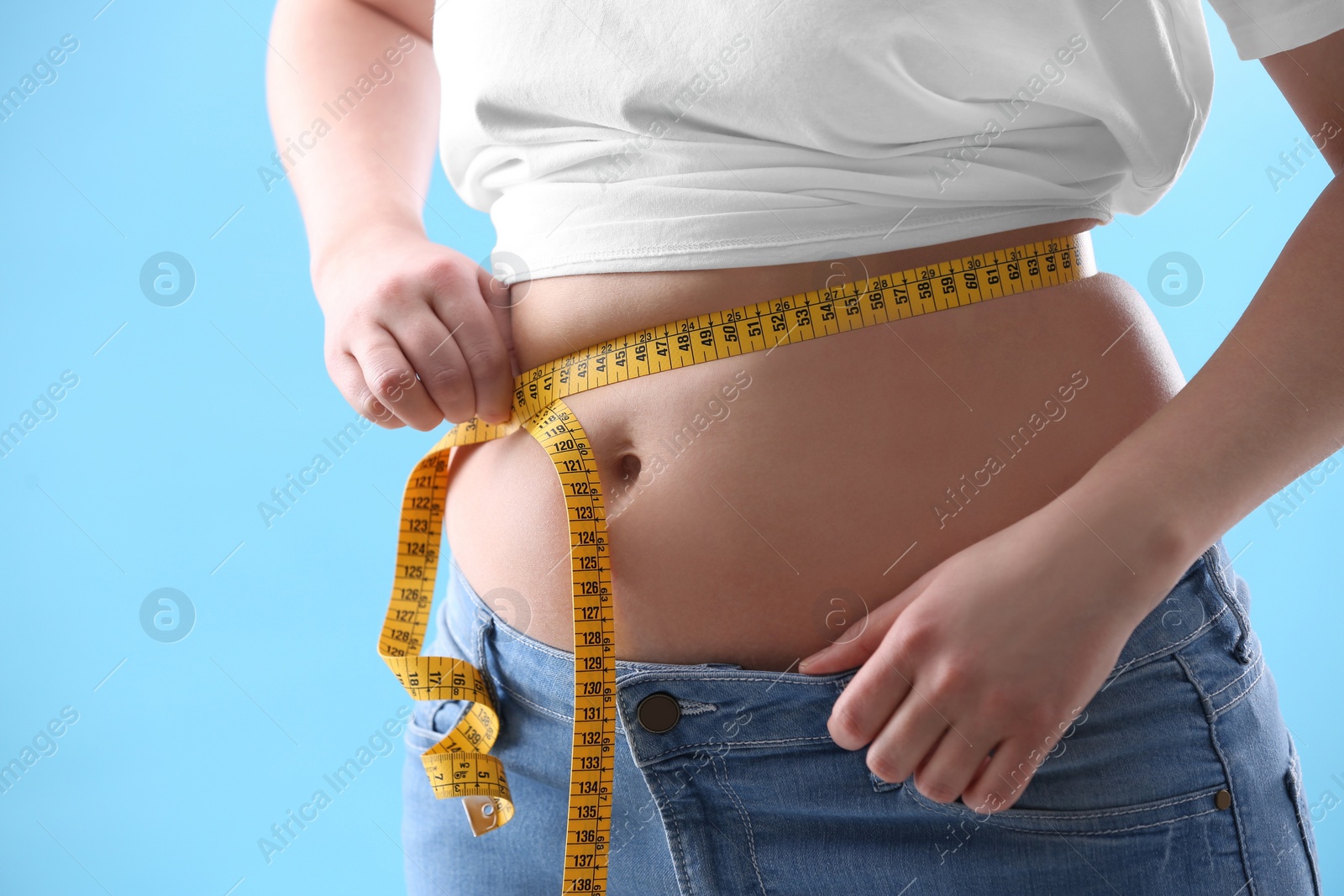 Photo of Woman with measuring tape on light blue background, closeup. Overweight problem after New Year party