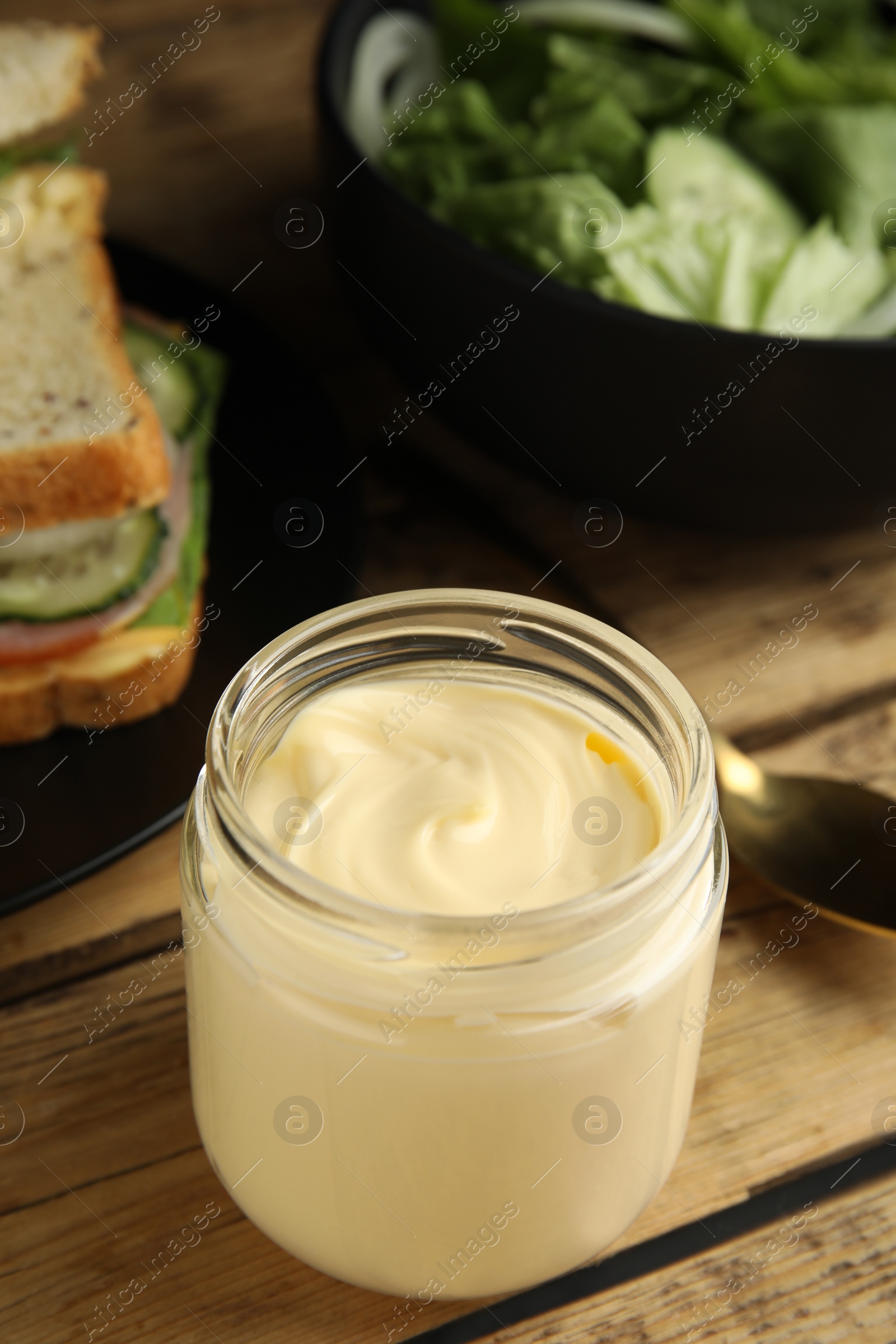 Photo of Jar of delicious mayonnaise near fresh sandwiches on wooden table