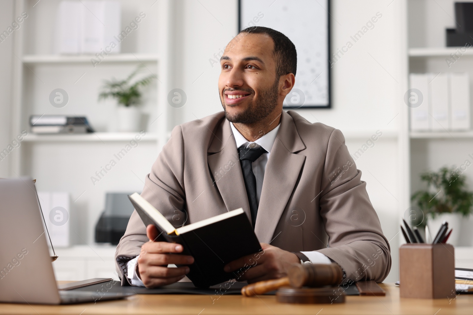 Photo of Smiling lawyer with book at table in office