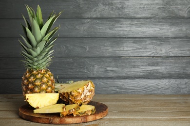 Photo of Whole and cut pineapples on wooden table. Space for text