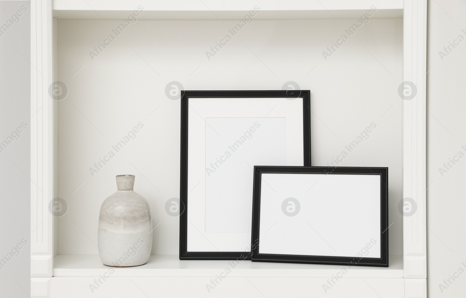 Photo of Blank frames and ceramic vase on shelving unit indoors