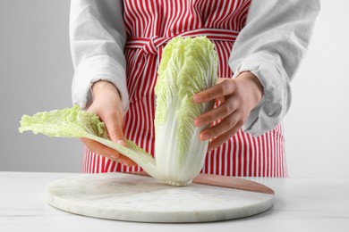 Woman separating leaf from fresh chinese cabbage at white marble table, closeup