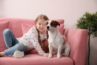 Cute little girl with her dog on sofa indoors. Childhood pet