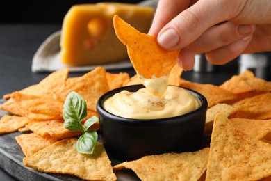 Photo of Woman dipping crispy nacho into delicious cheese sauce at table, closeup