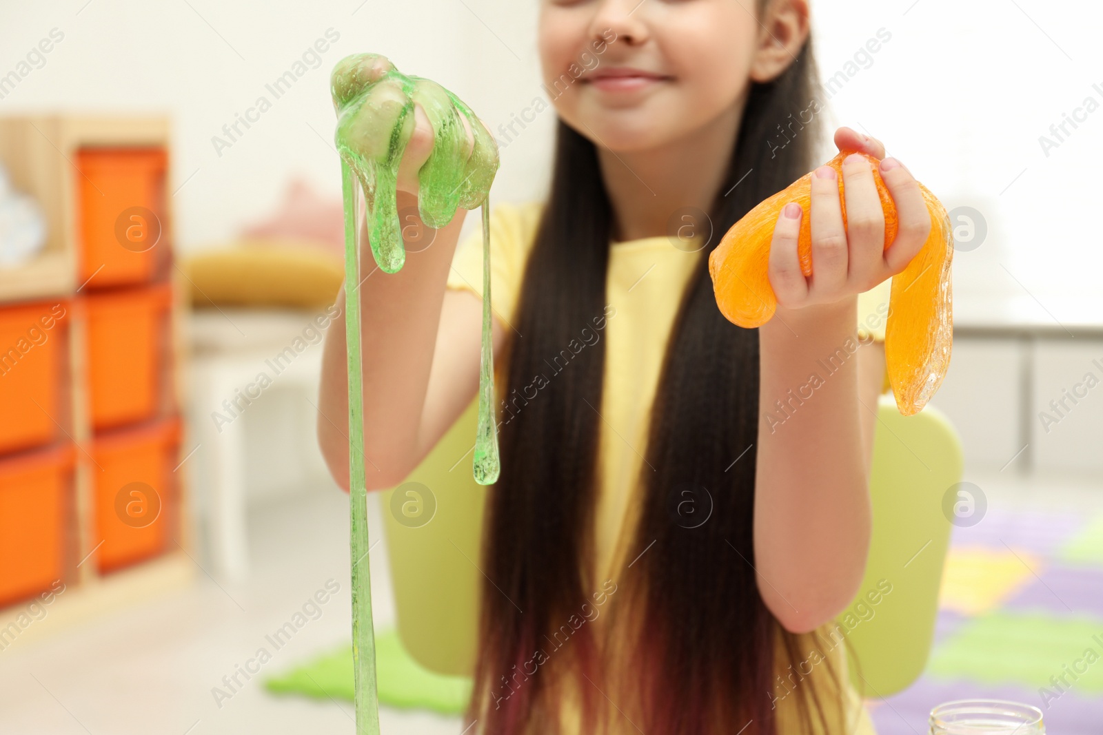 Photo of Little girl playing with slime in room, closeup