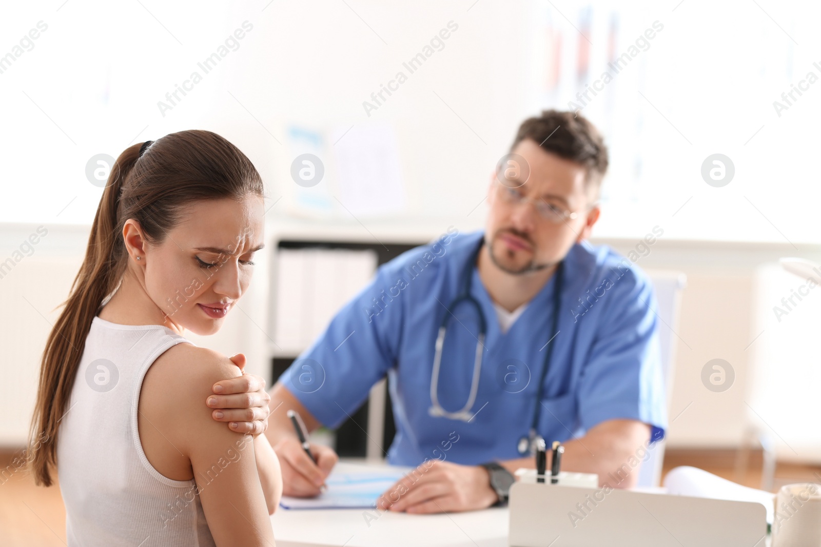 Photo of Male orthopedist examining patient with injured arm in clinic