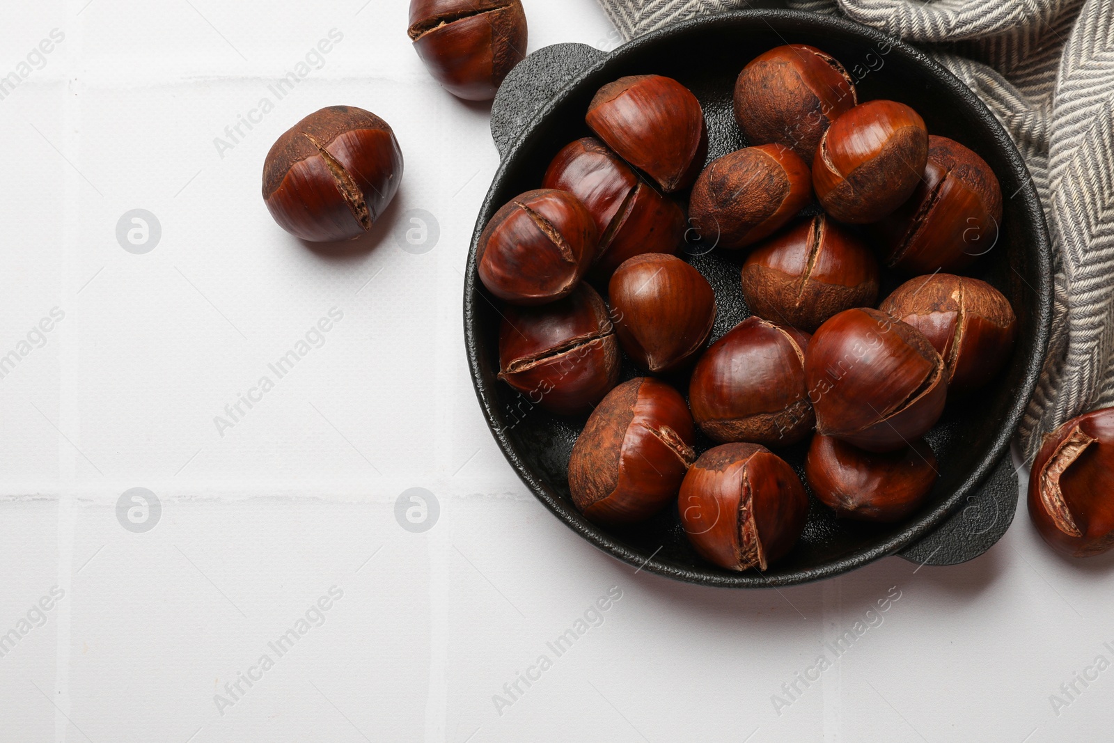 Photo of Fresh edible sweet chestnuts in frying pan on white tiled table, flat lay. Space for text