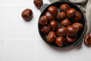 Photo of Fresh edible sweet chestnuts in frying pan on white tiled table, flat lay. Space for text