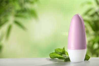 Photo of Deodorant container and mint on white wooden table against blurred background. Space for text