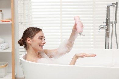 Woman pouring shower gel onto hand in bath indoors