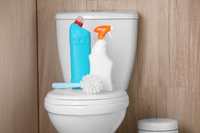 Photo of Bottles of cleaning products and brush on toilet bowl indoors