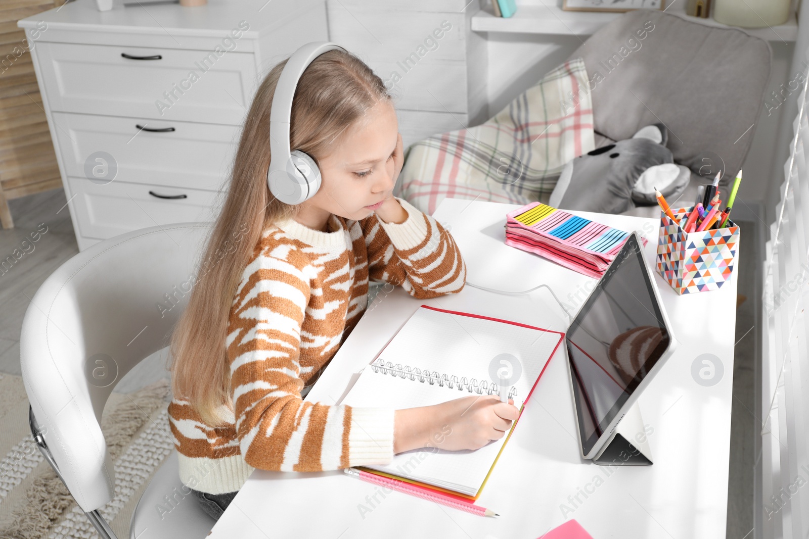 Photo of Cute little girl with modern tablet studying online at home. E-learning