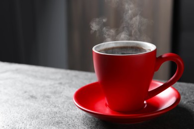 Image of Red cup with hot steaming coffee on grey table indoors, space for text
