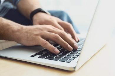 Man working on modern laptop at wooden table indoors, closeup