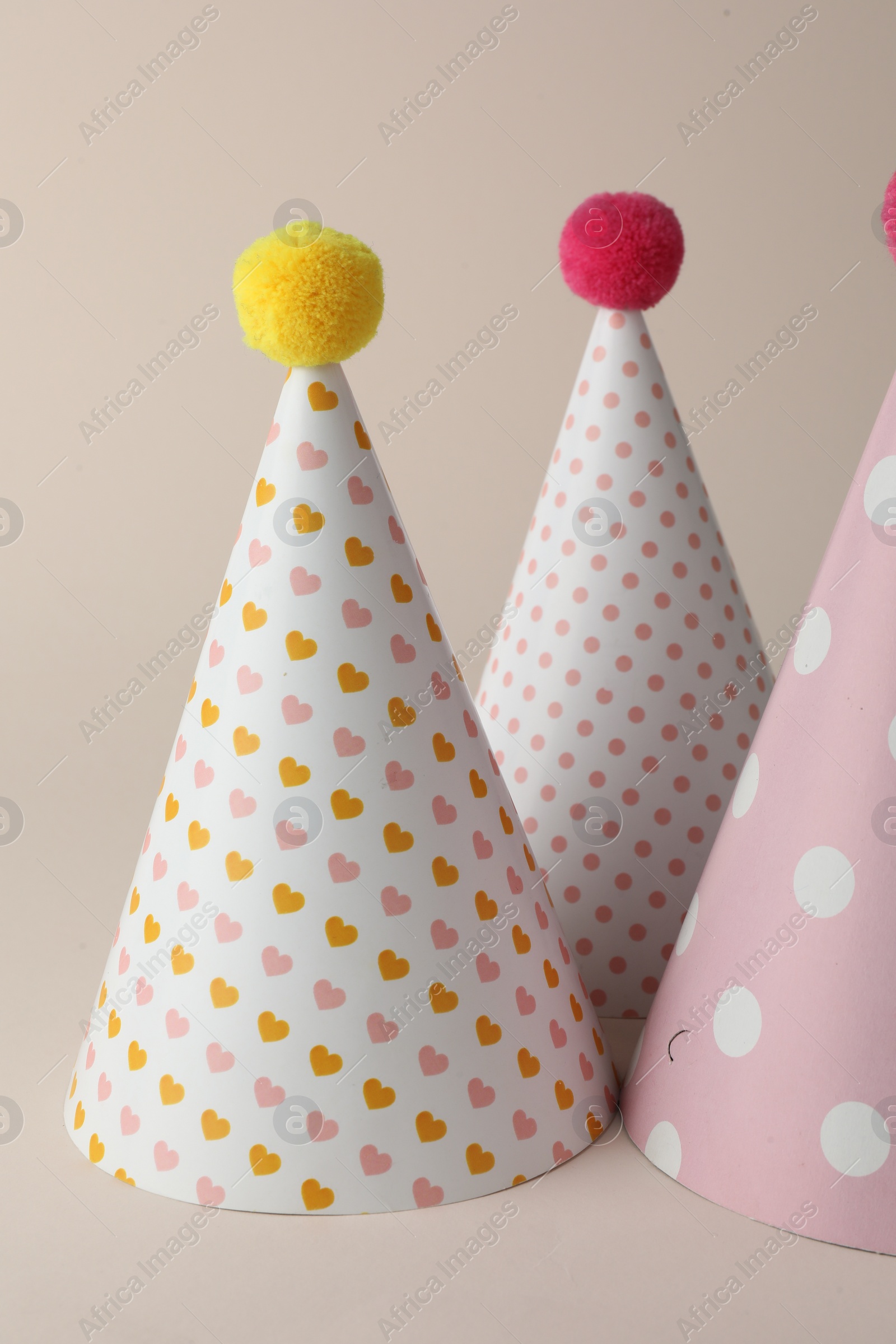 Photo of Beautiful party hats with pompoms on beige background