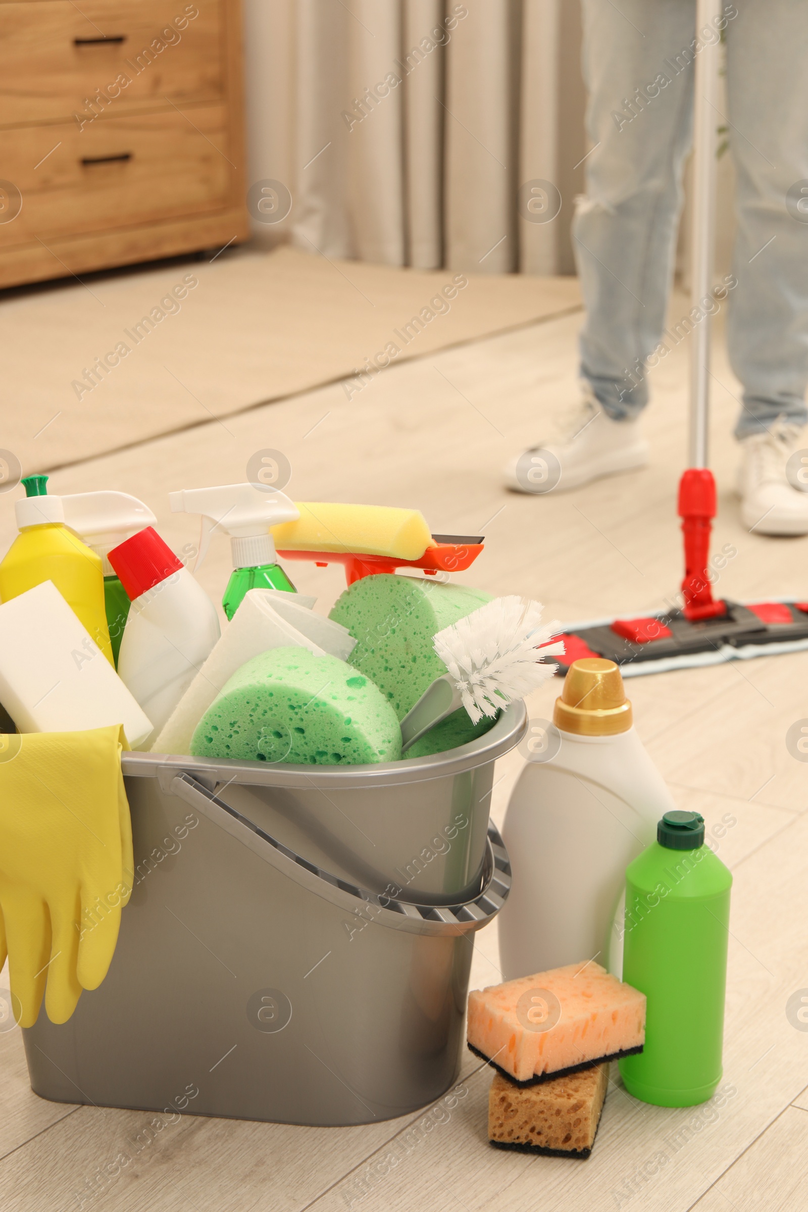 Photo of Different cleaning supplies in bucket and woman mopping floor, selective focus