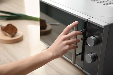 Young woman using microwave oven on table in kitchen