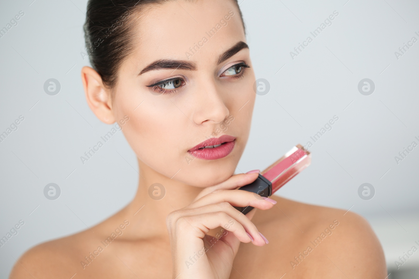 Photo of Young woman with liquid lipstick on light background