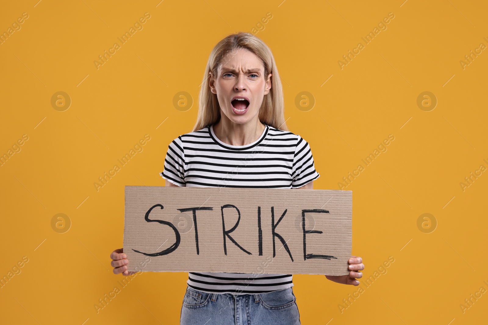 Photo of Angry woman holding cardboard banner with word Strike on orange background