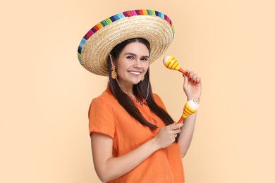 Photo of Young woman in Mexican sombrero hat with maracas on beige background