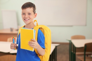 Image of Little boy with school stationery in empty classroom