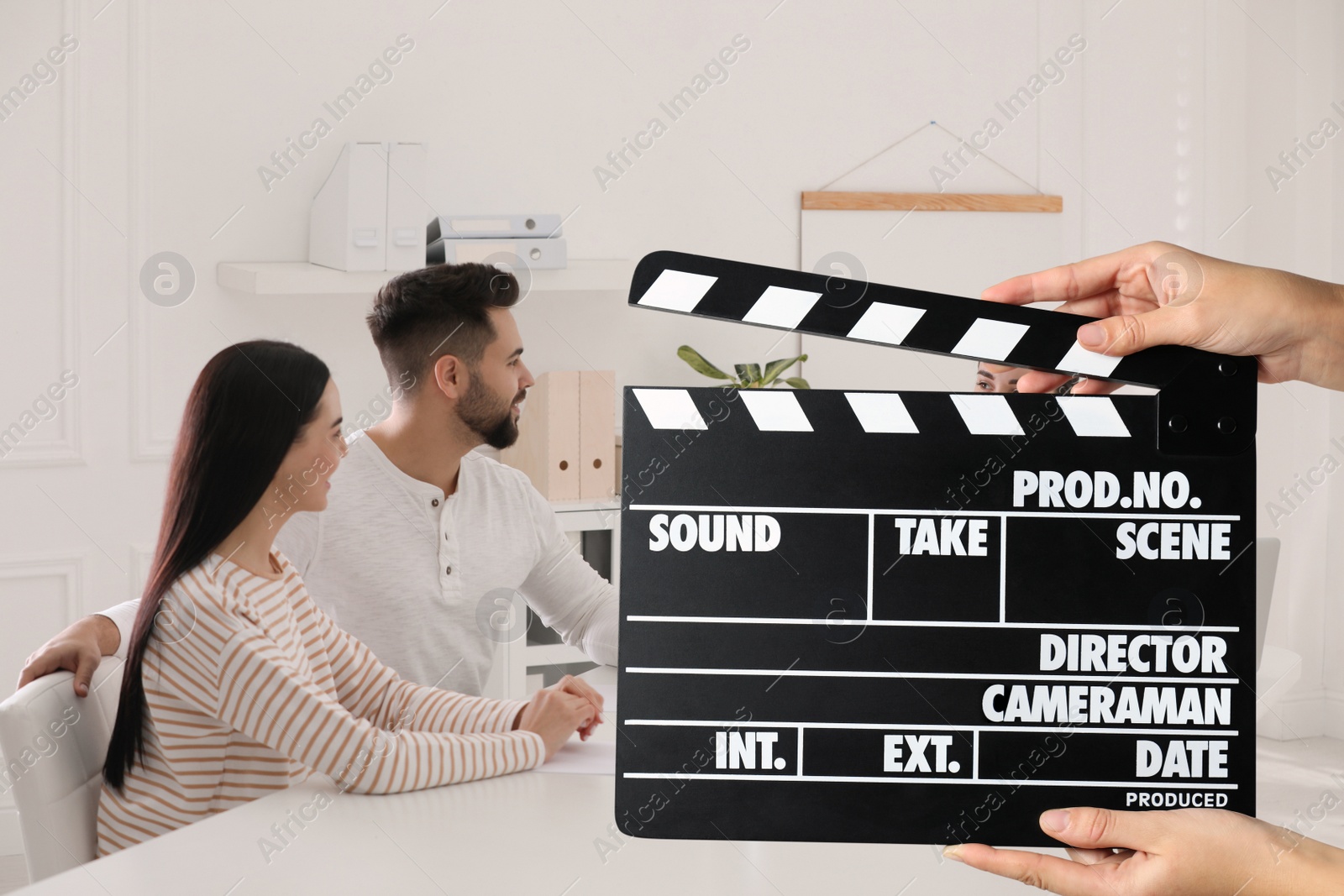 Image of Shooting movie. Second assistant camera holding clapperboard in front of actors at film set