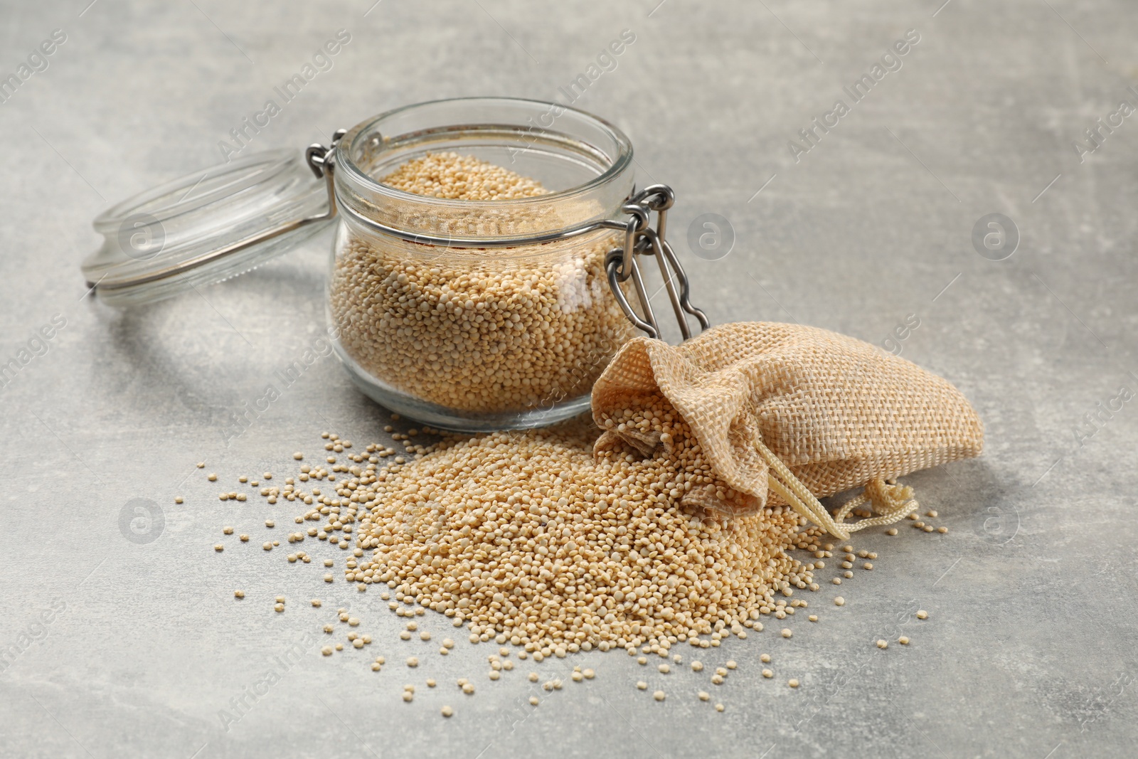 Photo of Dry quinoa seeds in glass jar and sack on light grey table