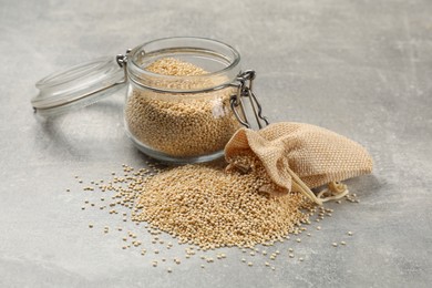 Photo of Dry quinoa seeds in glass jar and sack on light grey table