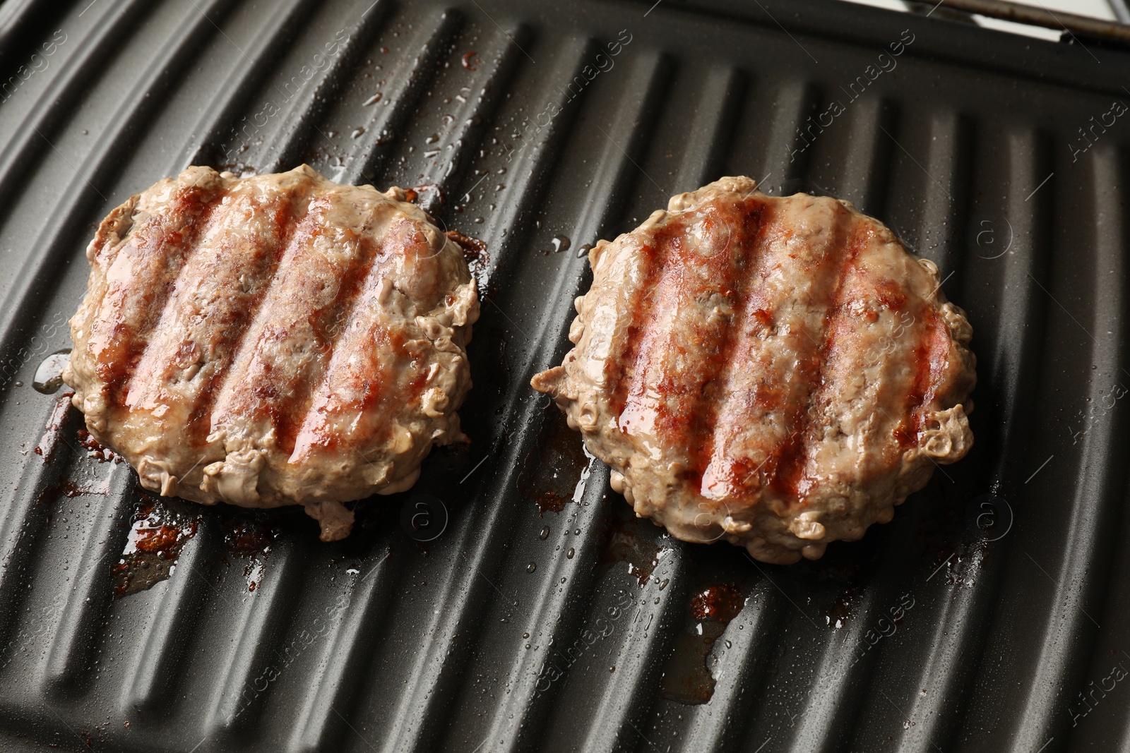 Photo of Delicious hamburger patties cooking on electric grill, closeup