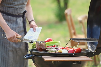 Young man cooking meat and vegetables on barbecue grill outdoors