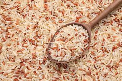 Photo of Mix of brown and polished rice with wooden spoon, top view