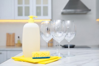 Photo of Clean glasses and cleaning product on table in stylish kitchen