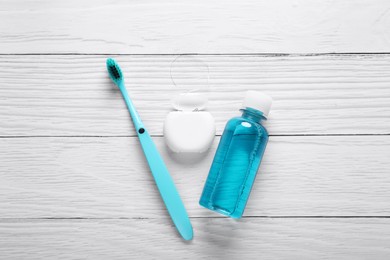 Dental floss, toothbrush and mouthwash on white wooden table, flat lay