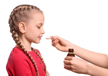 Mother giving syrup to her daughter from dosing spoon against white background