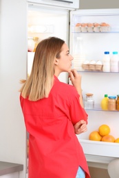 Thoughtful young woman choosing food from refrigerator in kitchen. Healthy diet