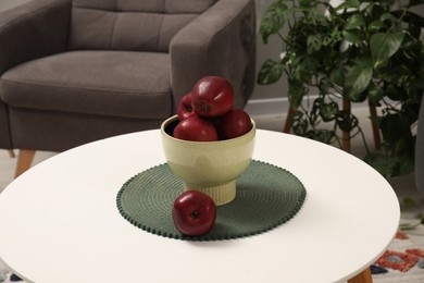 Photo of Red apples on coffee table near grey armchair indoors