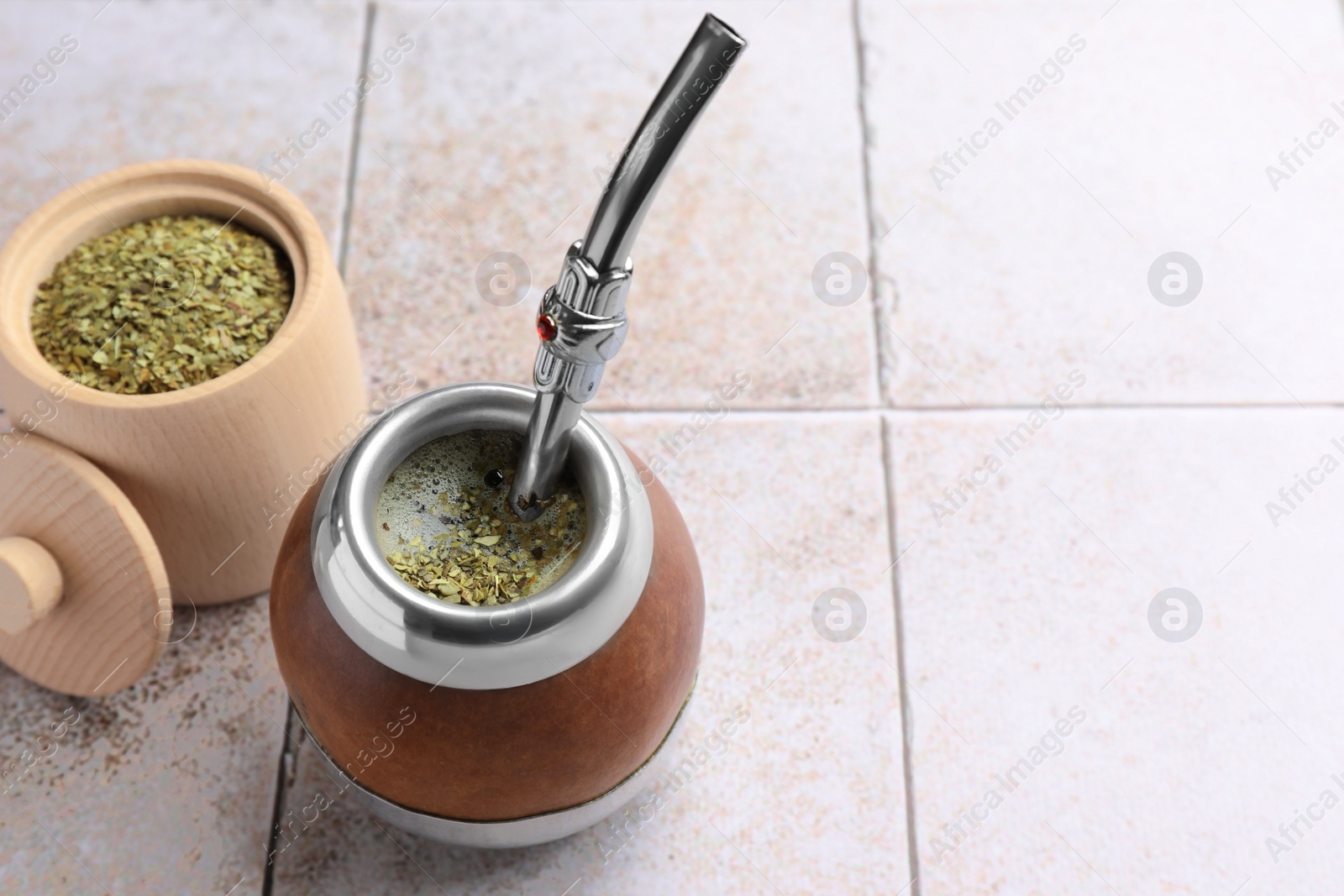 Photo of Calabash with bombilla and jar of mate tea leaves on tiled table, space for text