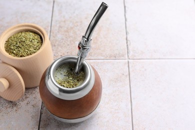 Photo of Calabash with bombilla and jar of mate tea leaves on tiled table, space for text