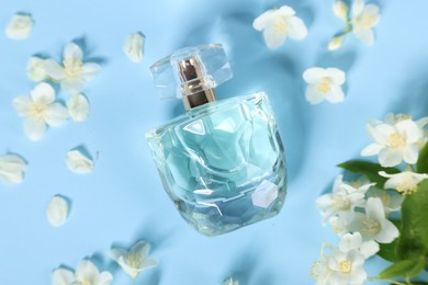 Aromatic perfume in bottle and beautiful jasmine flowers on light blue background, flat lay