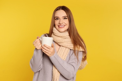 Photo of Beautiful young woman in sweater with drink on yellow background. Winter season