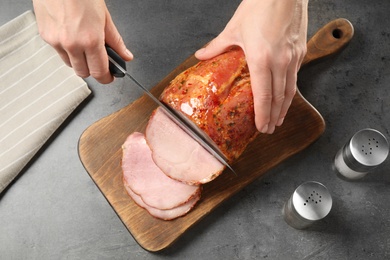 Woman cutting ham on wooden board at grey table, above view