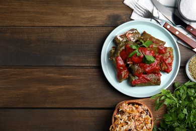 Photo of Plate of delicious stuffed grape leaves with tomato sauce, parsley and cutlery on wooden table, flat lay. Space for text