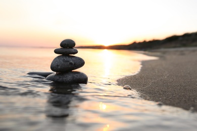 Photo of Dark stones on sand near sea at sunset, space for text. Zen concept