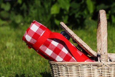 Photo of Rolled checkered tablecloth in picnic basket outdoors, closeup