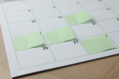 Photo of Timetable. Calendar page with green sticky notes on wooden table, closeup