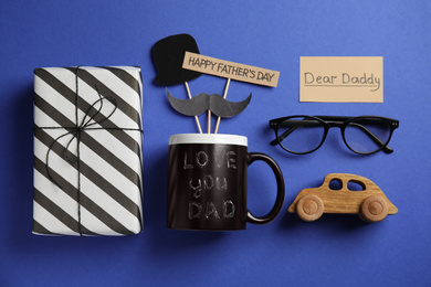 Photo of Flat lay composition of gift box and eyeglasses on blue background. Happy Father's day