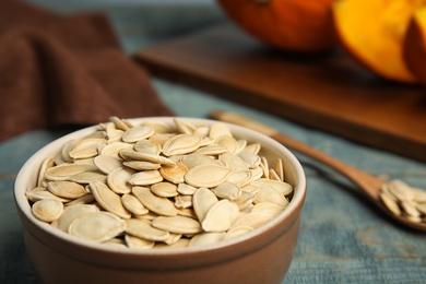 Photo of Bowl of raw pumpkin seeds on blue wooden table, closeup. Space for text