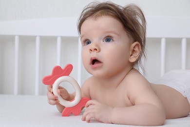 Photo of Cute little baby with teether in comfortable crib at home